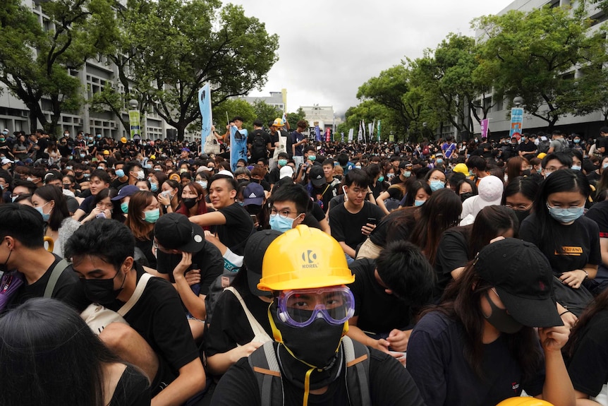 A group of hundreds of people wearing black shirts, helmets and face masked.