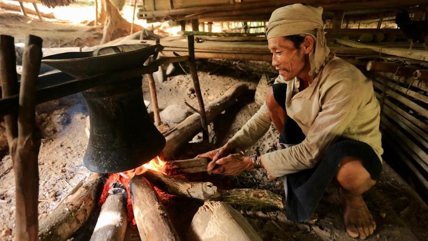A man burning wood to cook using a big traditional pot