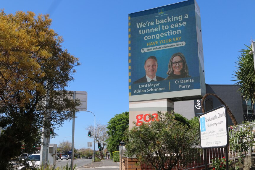 An image of a blue billboard featuring two people and the words 'We're backing a tunnel to ease congestion'.