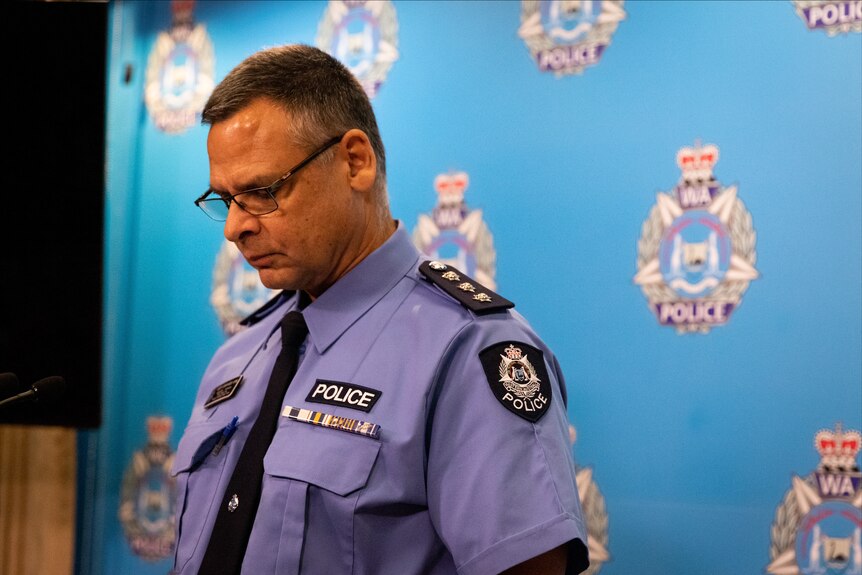 A police officer in full uniform bows his head in front of a WA Police backdrop