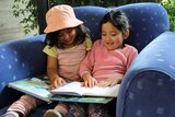 Two young girls read a story together at the library.