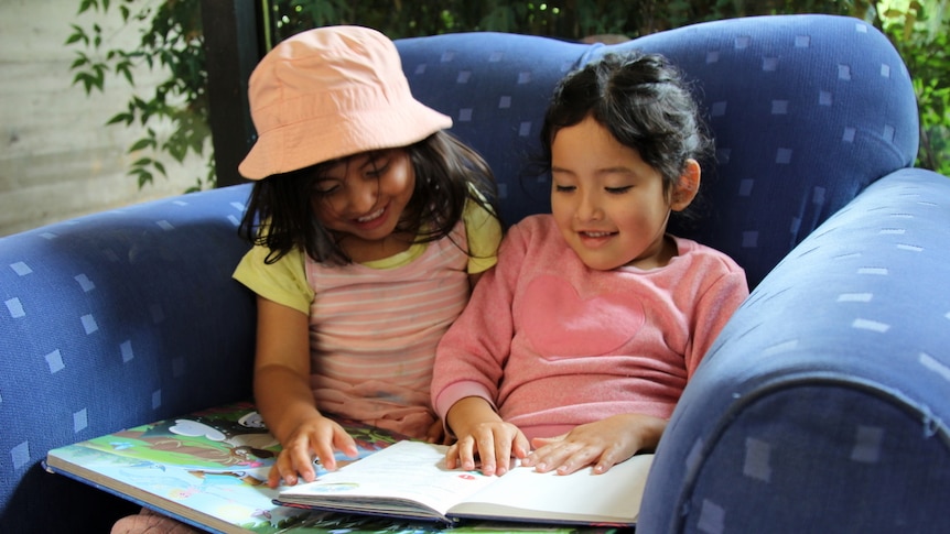 Two young girls read a story together at the library.