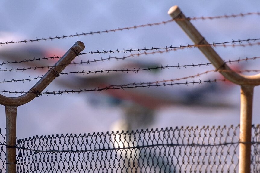 A barbed wire fence, Sydney Airport is out of focus in the background.