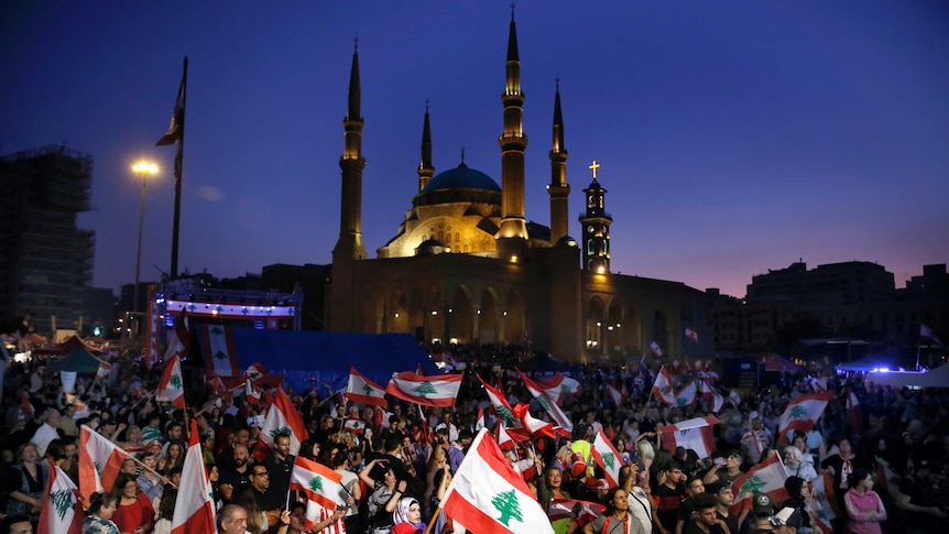 Anti-government protesters hold national flags during a twilight rally outside a mosque in Beirut.