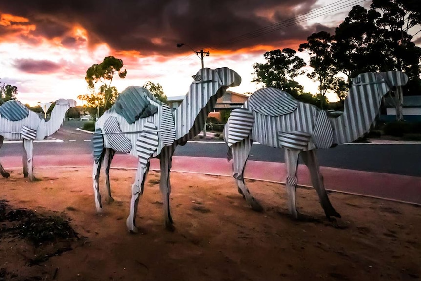 Four metal camels with a cloudy sky above them.