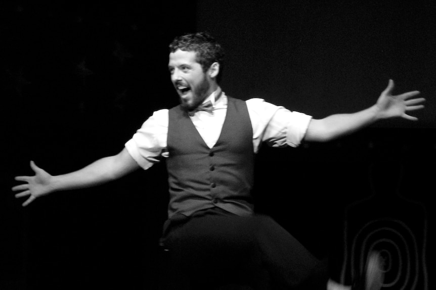 Caleb spreads his hands as he sings and dances on stage, in a black-and-white photograph.