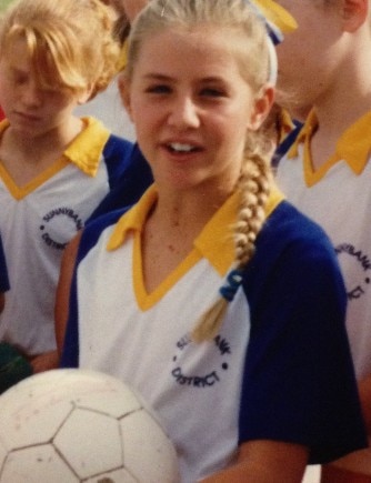 Stacey Marinkovich holds a netball while posing for a photo in a yellow and blue netball outfit.