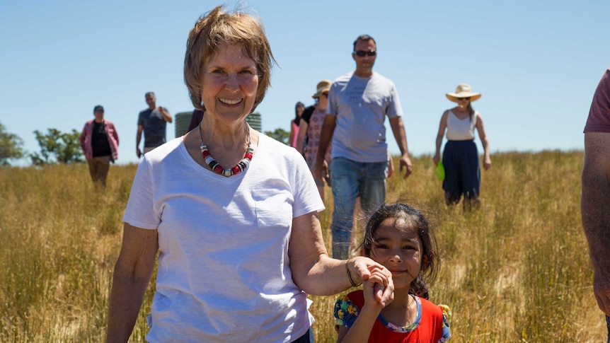 A woman walks hand-in-hand with a young asylum seeker child through a paddock in the Adelaide Hills.