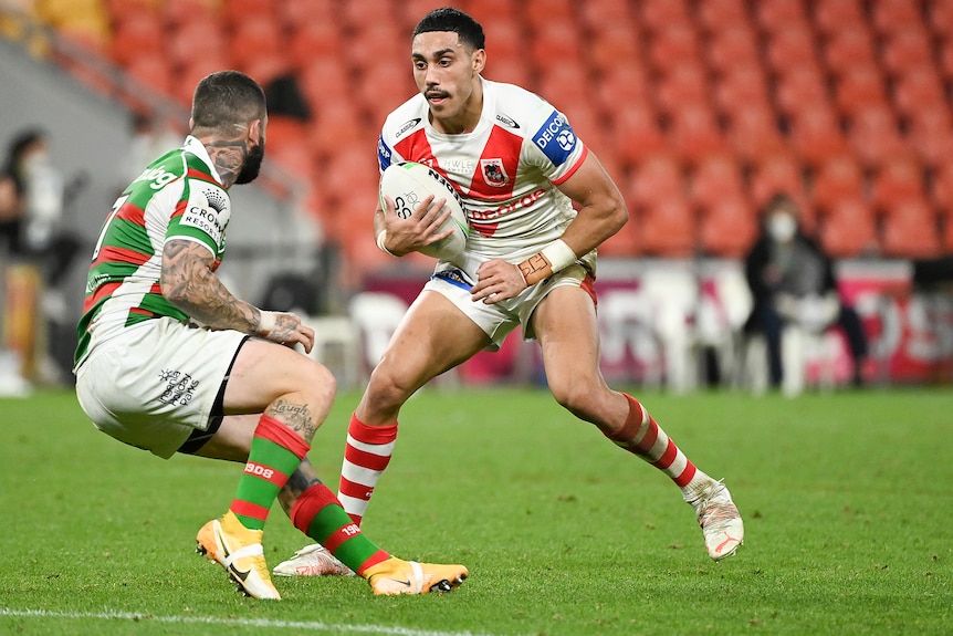 A player from St George Illawarra NRL holds the ball with his right hand as he tries to beat a defender from South Sydney.