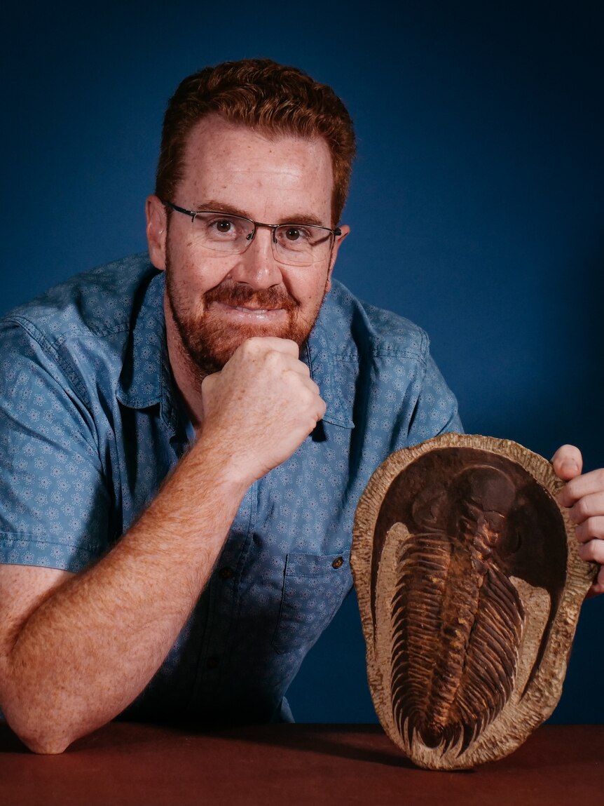 A man with glasses holding a trilobite fossil