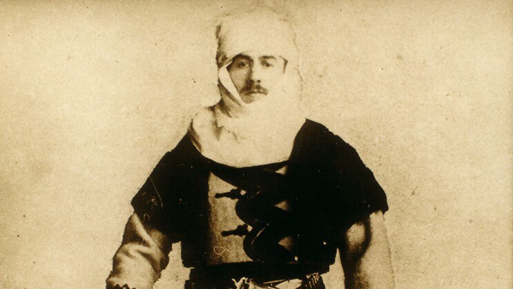 A sepia photograph of a man in Albanian clothing holding a gun