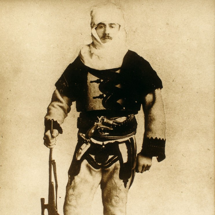 A sepia photograph of a man in Albanian clothing holding a gun
