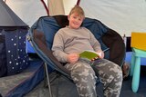 A smiling boy sits on a large chair in a tent, reading a Dr Seuss book.
