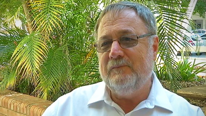 A head shot of a man with a white beard and glasses wearing a white shirt