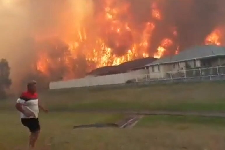 A man runs in front of a fire threatening homes