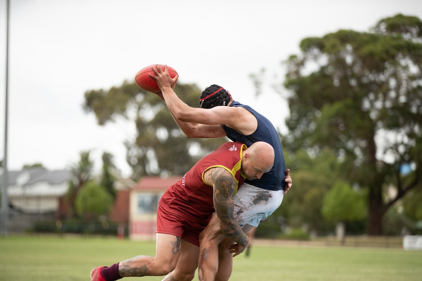 bald man tackles man marking ball