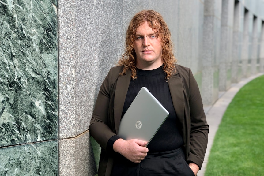 a red-headed woman holing a laptop, in a brown blazer