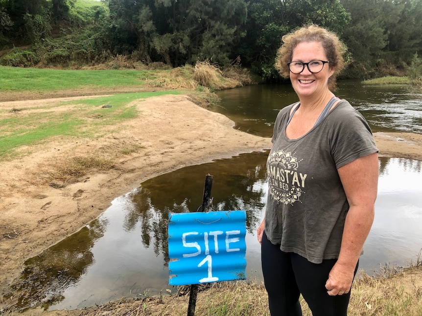 Smiling women stands in front of flooded campsite with blue 'campsite 4' sign