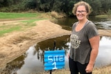 Smiling women stands in front of flooded campsite with blue 'campsite 4' sign