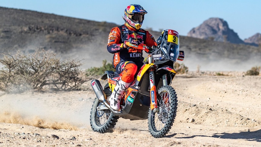 Sand flies up as a motorcyclist speeds through rocky terrain on the first leg of a rally race.