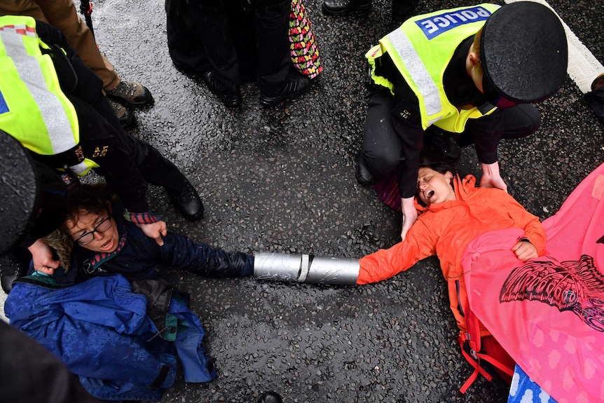 Police officers attempt to remove climate change activists who have locked their hands together