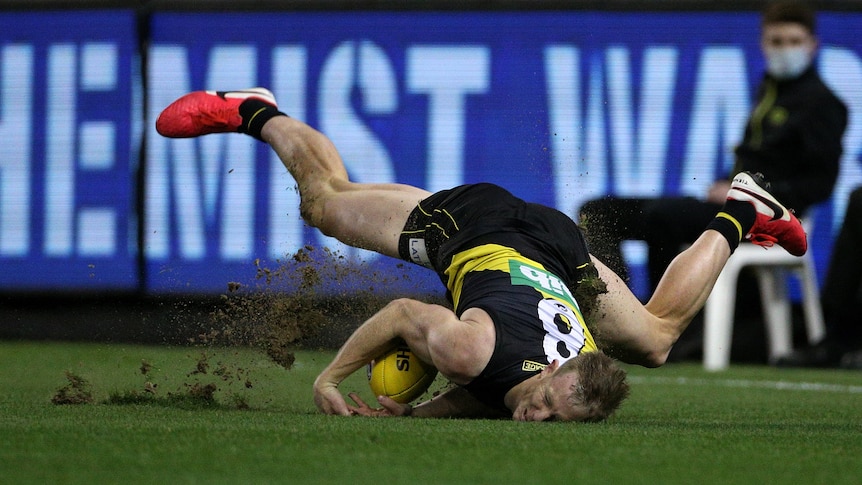 A Richmond Tigers AFL player lands on the playing surface via his head as he attempts to mark the ball.