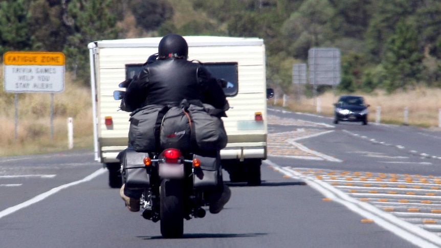 A motorcyclist follows behind a car and caravan on the Bruce Highway.