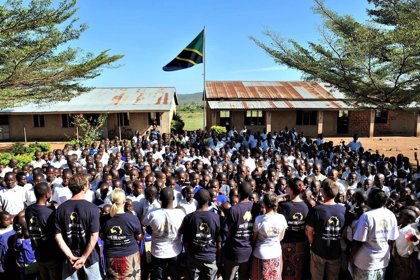 Hundreds of African school students standing outside their school, looking at a group of western volunteers.