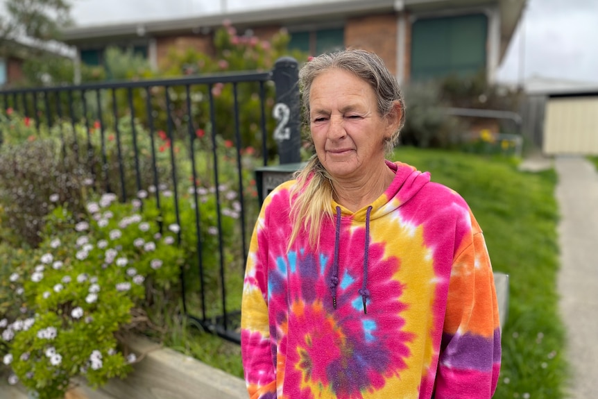 Dianne stands in a colourful jumper outside her home