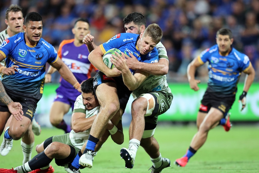 Rugby union player running the ball with opposition players trying to tackle him during a match