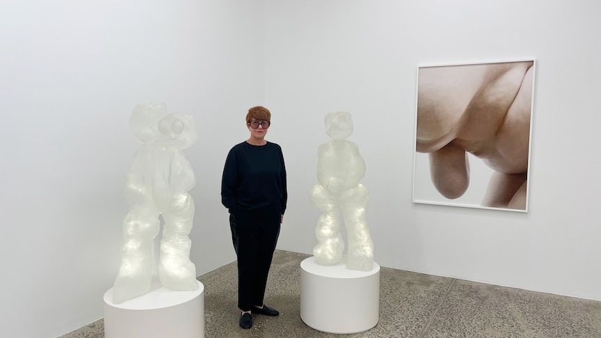 A woman in dark clothes standing between two white statues and hear an abstract photo on the wall