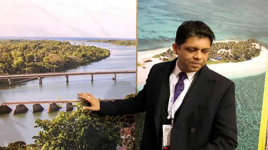 A man gestures while speaking in front of photos of low-lying Pacific islands