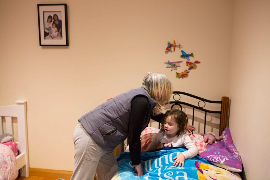 Sue Erben puts her granddaughter, Jayde, to bed.