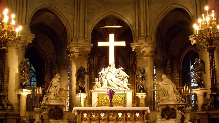 A statue and cross is illuminated inside a cathedral