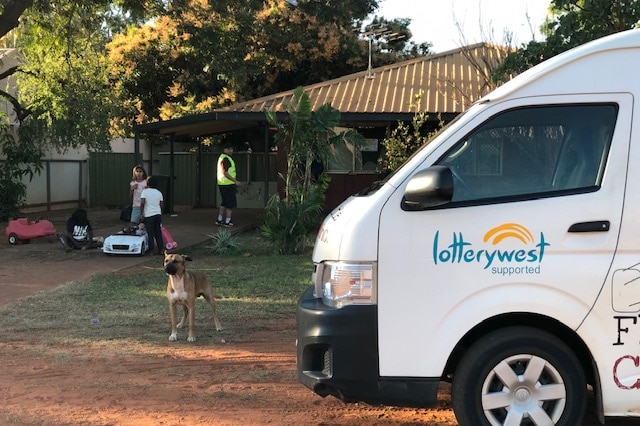 A white bus in front of a house with a dog and several people standing in the driveway