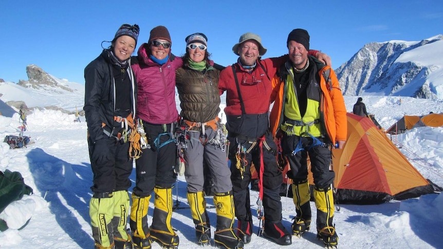 five climbers in line for a photo high on snowy mountain summit