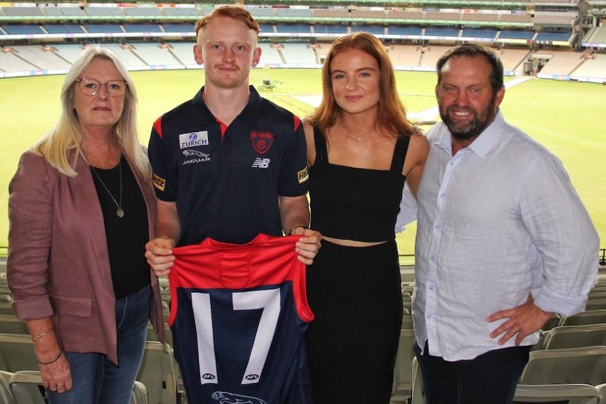 A Melbourne AFL player pictured holding a Demons jersey with his family at the MCG.