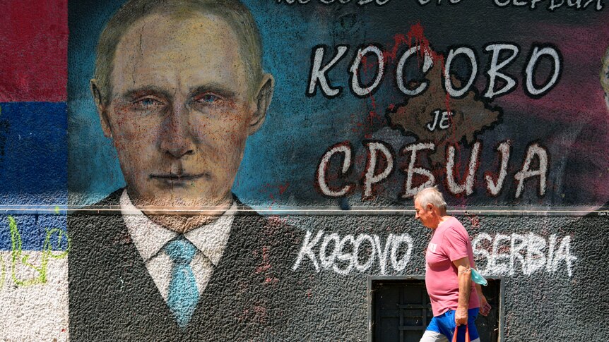 A man passes by graffiti on a wall depicting Russian President Vladimir Putin and the words "Kosovo is Serbia".