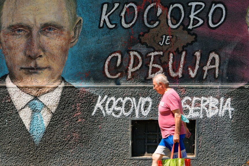 A man passes by graffiti on a wall depicting Russian President Vladimir Putin and the words "Kosovo is Serbia".