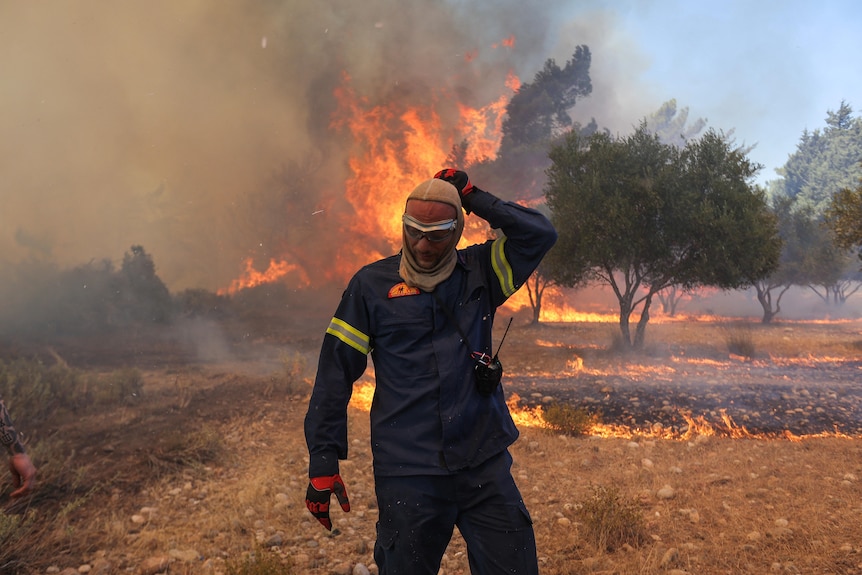 A firefighter walks next to rising flames as a wildfire burns on the island of Rhodes, Greece.