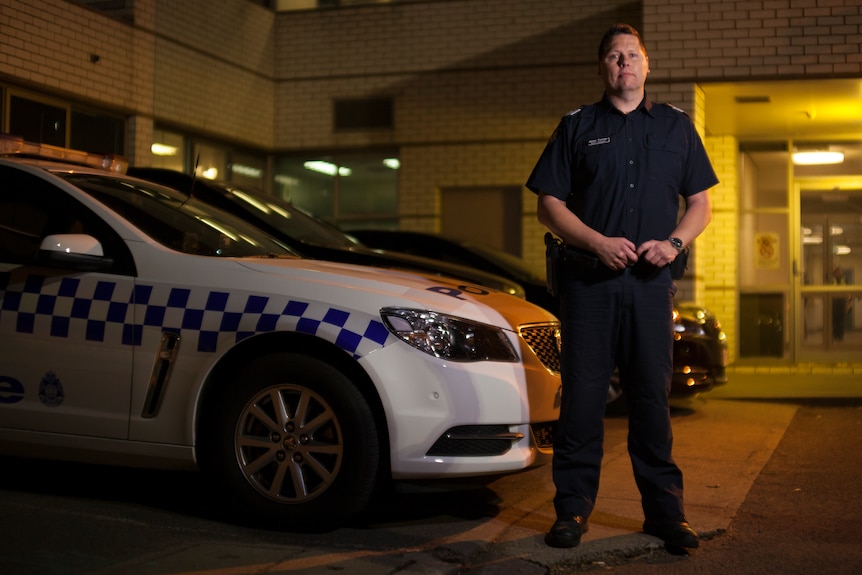 Senior Sergeant Jason Forster stands in front of a police car.