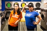 Two women stand proudly in front of washing machines and dryers