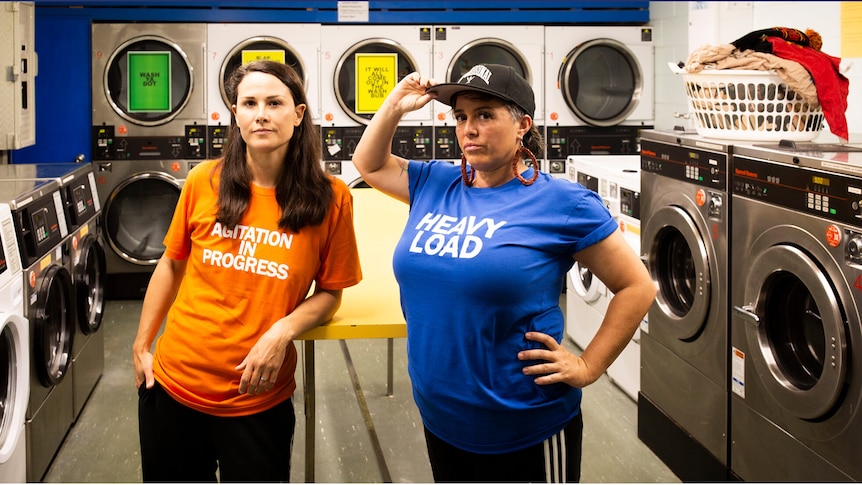 Two women stand proudly in front of washing machines and dryers