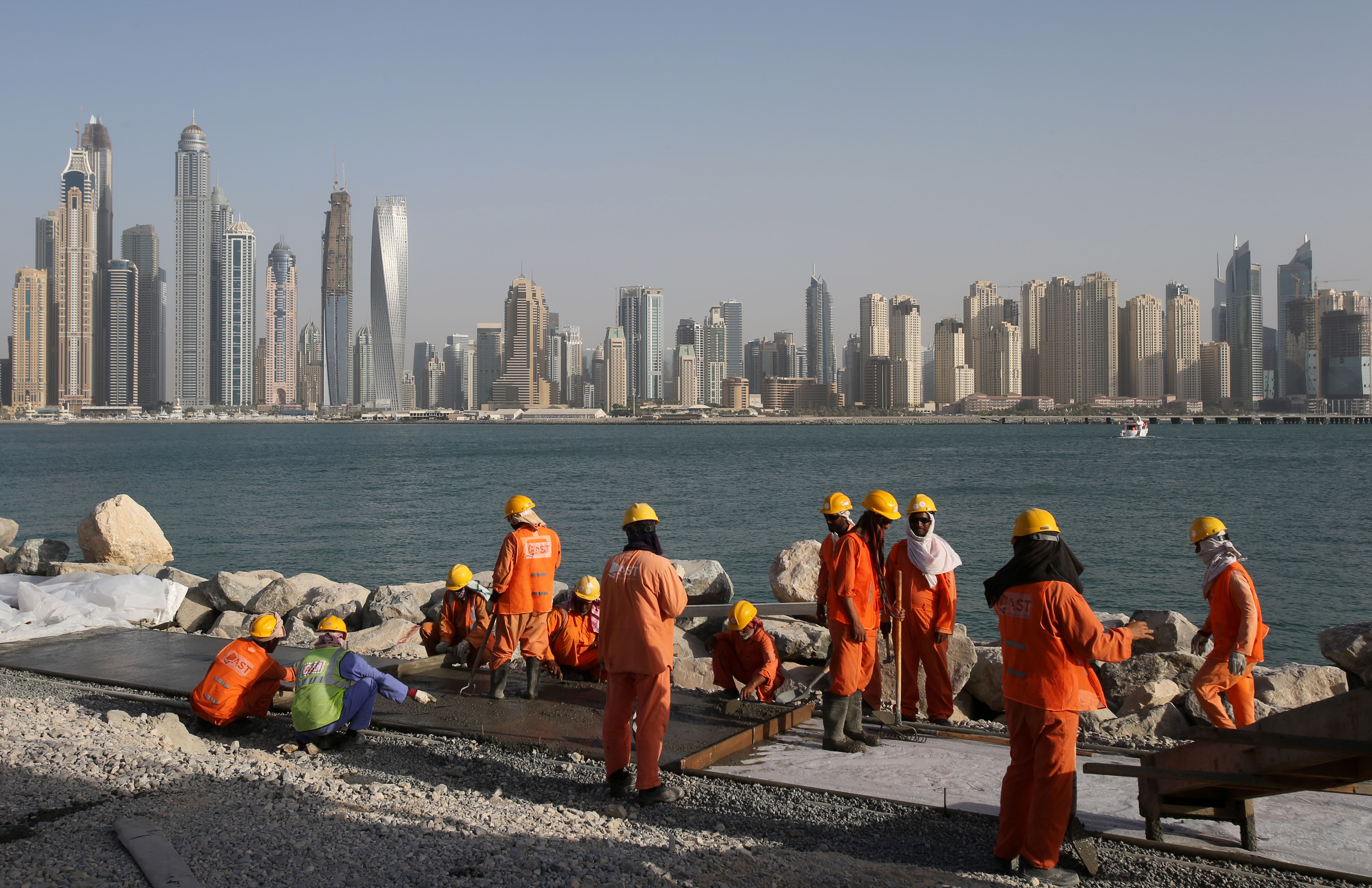 Trabajadores vestidos con trajes naranjas trabajan en un sitio de construcción con el horizonte de Dubai al fondo 