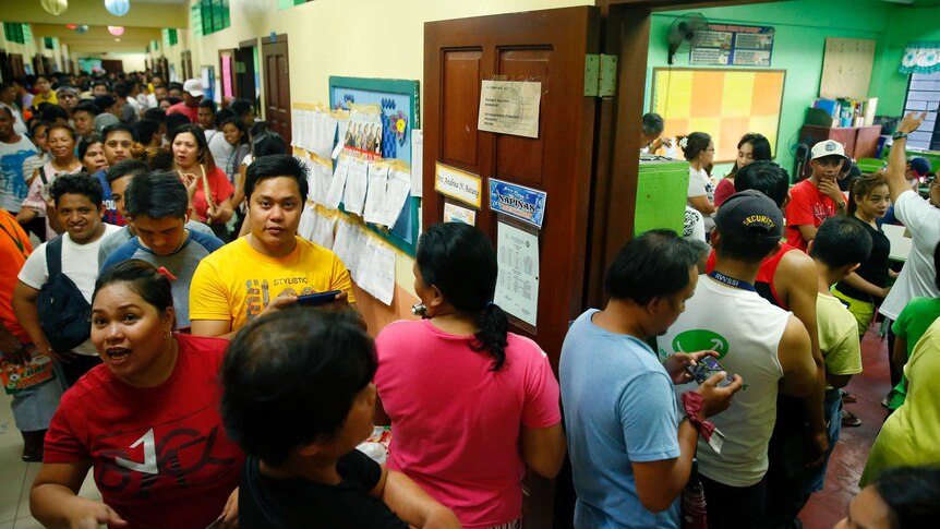 People queue up outside a polling precinct to vote in the Philippine midterm elections.