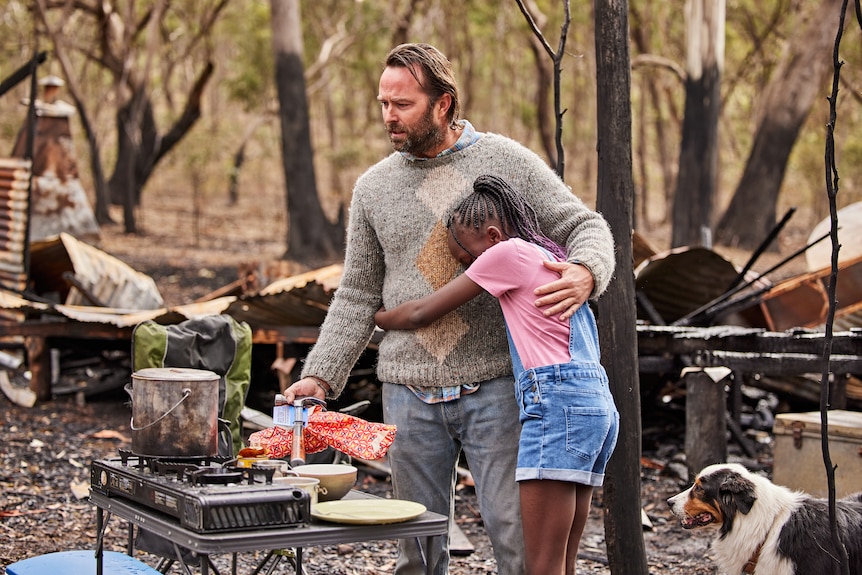 A young girl hugs a man in the remains of a burnt house.
