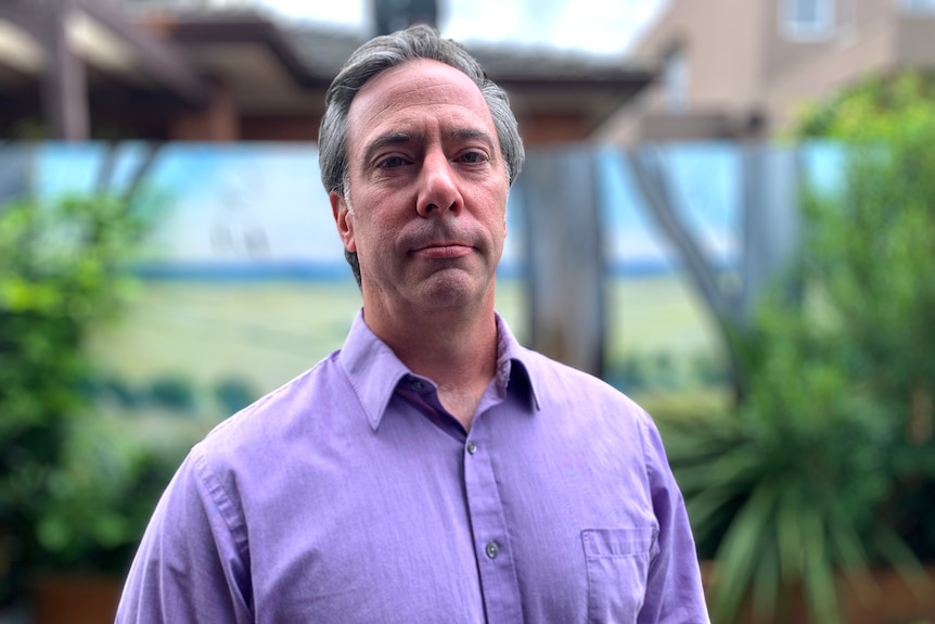 A man looking into the camera, standing outside.