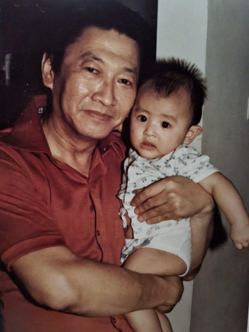 A baby photo of Christian with his father. His father is holding him and smiling.