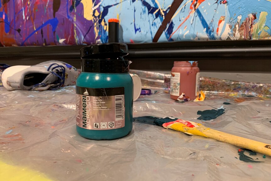 Paint bottles and brushes sit on ground in front of graffiti art in gallery.