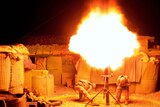 Two United States soldiers block their ears as they fire a mortar round at night in Afghanistan